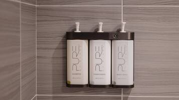 Three bottles of PURE shampoo, conditioner, and body wash mounted on a tiled wall.
