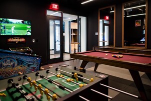 Una habitación con mesa de billar, mesa de fútbol de mesa y una televisión mostrando un partido de golf.
