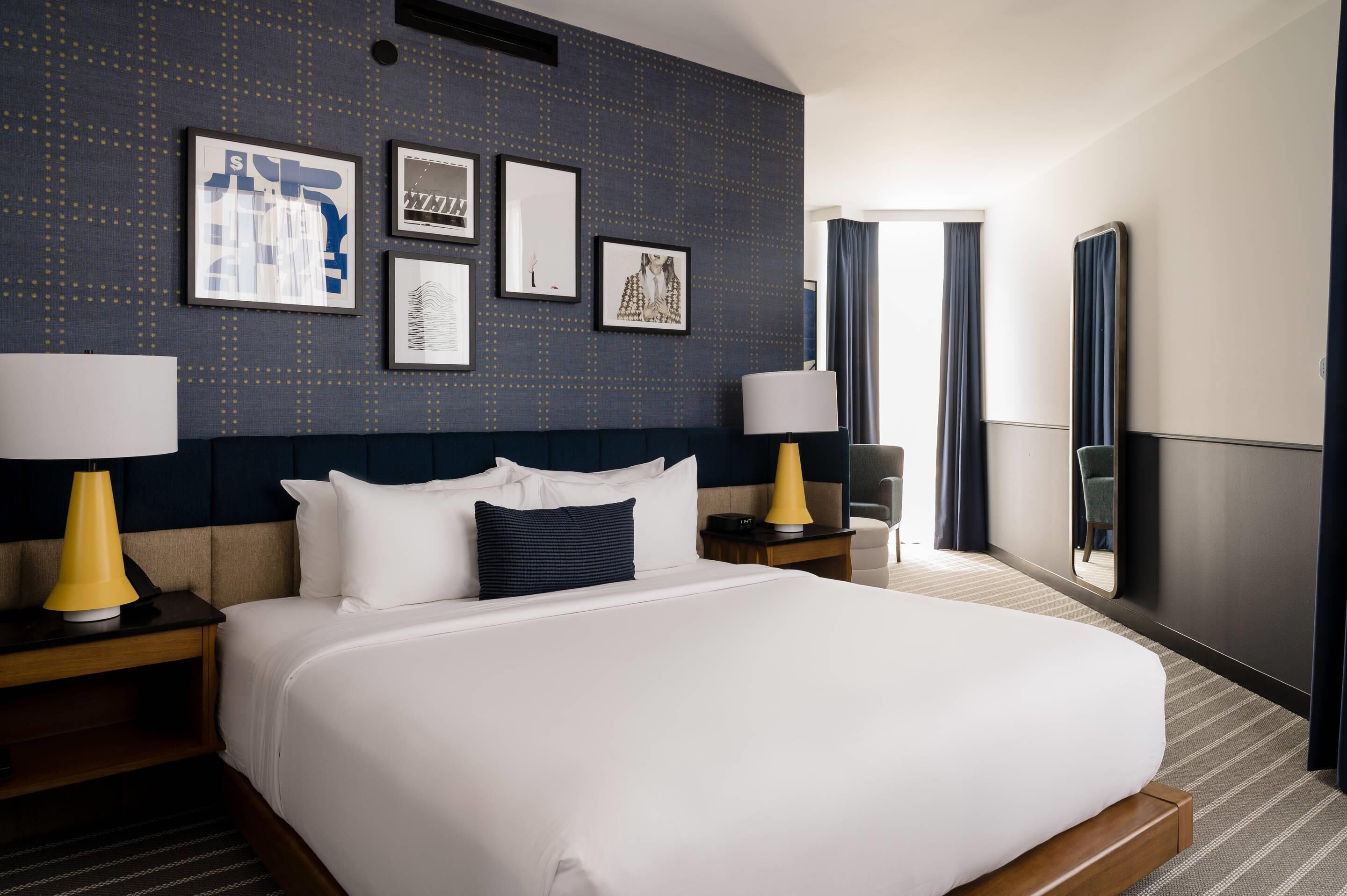 A hotel room with a large bed, two bedside tables with lamps, a dark headboard, and framed artwork on the wall.