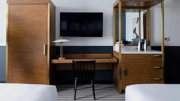 Quarto de hotel com uma escrivaninha de madeira, uma cadeira, televisão, frigobar e uma cama.