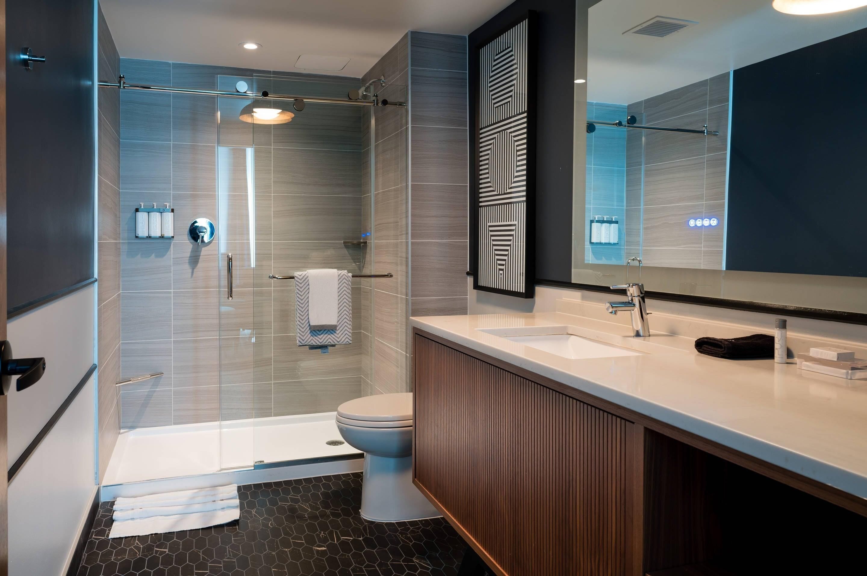 Ein modernes Badezimmer mit Duschkabine aus Glas, Toilette, Waschtisch mit Spiegel und Waschbecken.