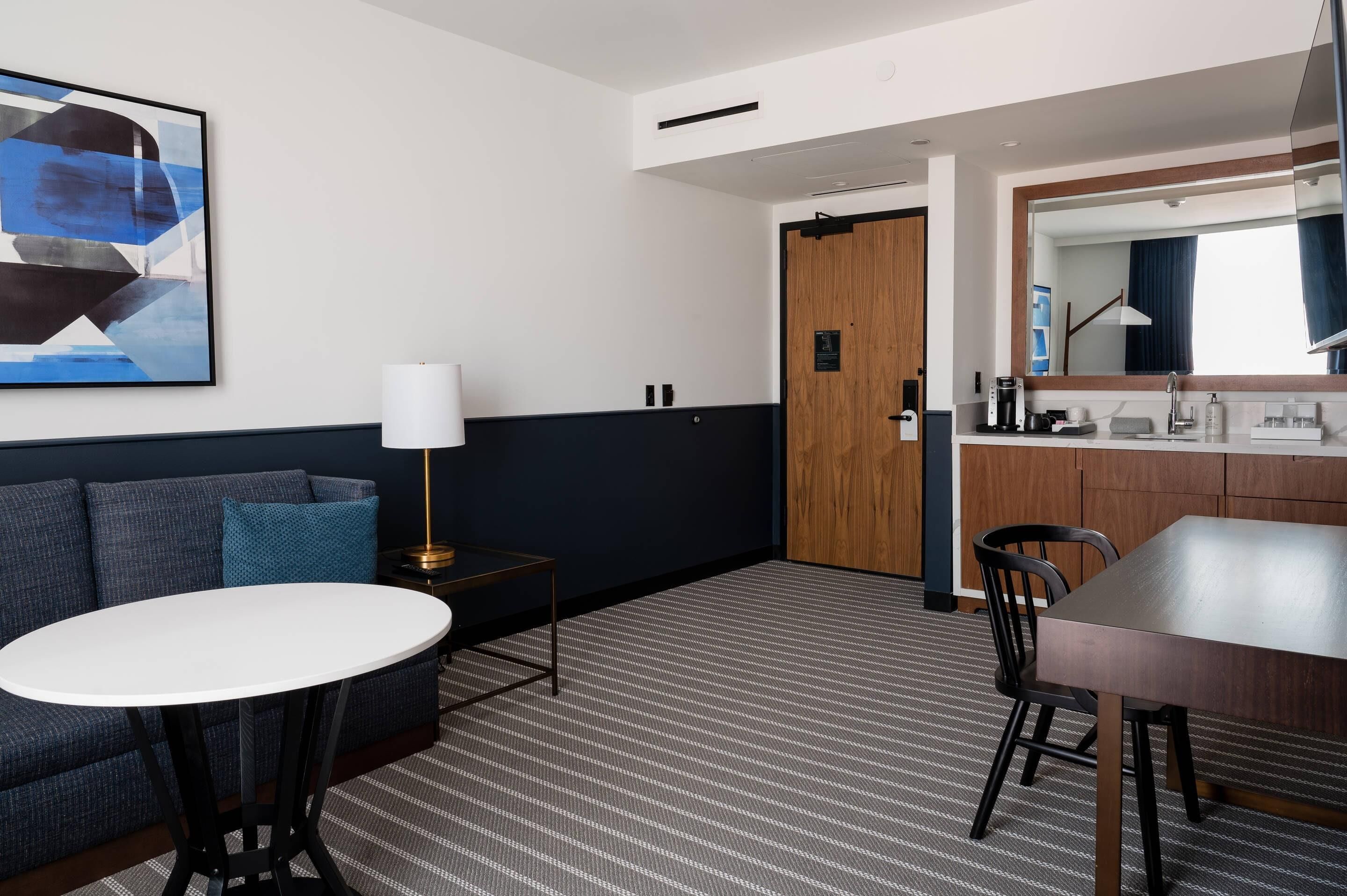 Habitación de hotel con sofá, una mesa redonda, una cafetera y un espejo.