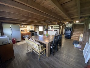 Uma cozinha espaçosa com vigas de madeira, uma área de jantar com uma mesa grande e cadeiras, e uma sala de jantar separada com uma escada.