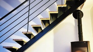 A modern staircase with a black railing and wooden steps, a green chair, and a wood-burning stove. - Loft in the heart of the vineyards in a former Chai dating from 1815 (Marcy)