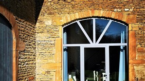 A stone building with a large arched window and a glass door. There are two lounge chairs outside on the grass. - Loft in the heart of the vineyards in a former Chai dating from 1815 (Marcy)