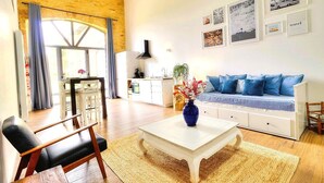 A living room with a sofa, coffee table, and a dining area with a table and chairs. - Loft in the heart of the vineyards in a former Chai dating from 1815 (Marcy)