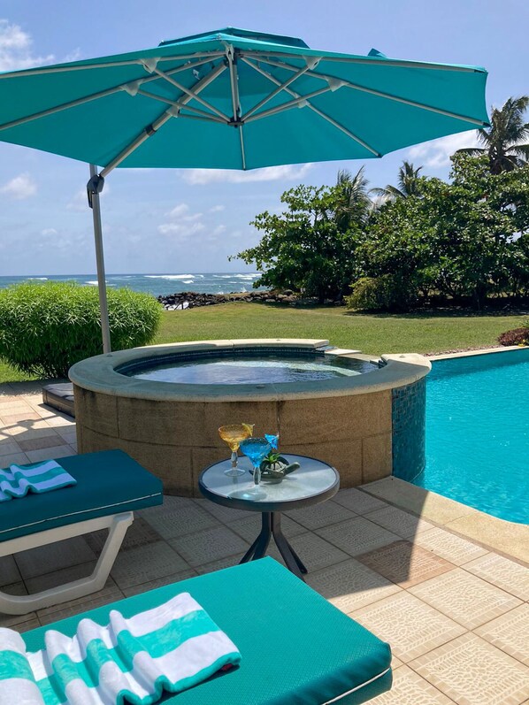 Zona de piscina con hidromasaje, sillas de descanso y una mesa con bebidas.