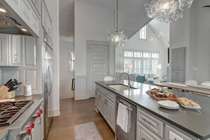 A modern kitchen with white cabinetry, stainless steel appliances, and a large island with a sink and dining area.
