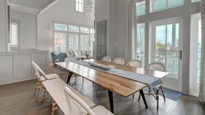 Een ruime eethoek met een lange houten tafel, witte gestoffeerde stoelen en een bank.