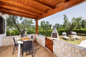 An outdoor patio with stone walls, a wooden ceiling, and a stone fireplace. There are two lounge chairs and a table with breakfast items. - Detached  Villa, 55 square meters, on the ground floor with private garden of 150 square meters with barbecue and sunbeds (Vieste)