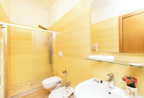 A bathroom with a glass shower enclosure, a white toilet, a sink with a glass shelf above it, and a mirror with a wooden cabinet above. - Detached  Villa, 55 square meters, on the ground floor with private garden of 150 square meters with barbecue and sunbeds (Vieste)