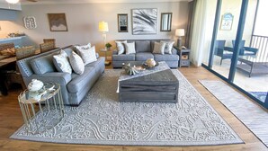 A spacious living room with a grey sofa, a coffee table, and a large window offering a view of outdoor furniture. - Sanibel Harbour Resort Harbour Tower 814:    Renovated waterfront condo with beach, pool, grill (Fort Myers)