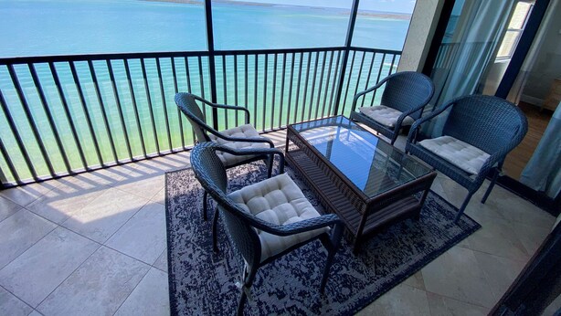 A balcony with a glass table and wicker chairs, overlooking a clear blue sea. - Sanibel Harbour Resort Harbour Tower 814:    Renovated waterfront condo with beach, pool, grill (Fort Myers)