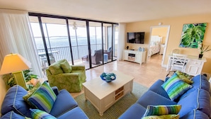 Un salon comprenant un canapé, une table basse et un téléviseur. Il y a un balcon avec vue sur la mer.