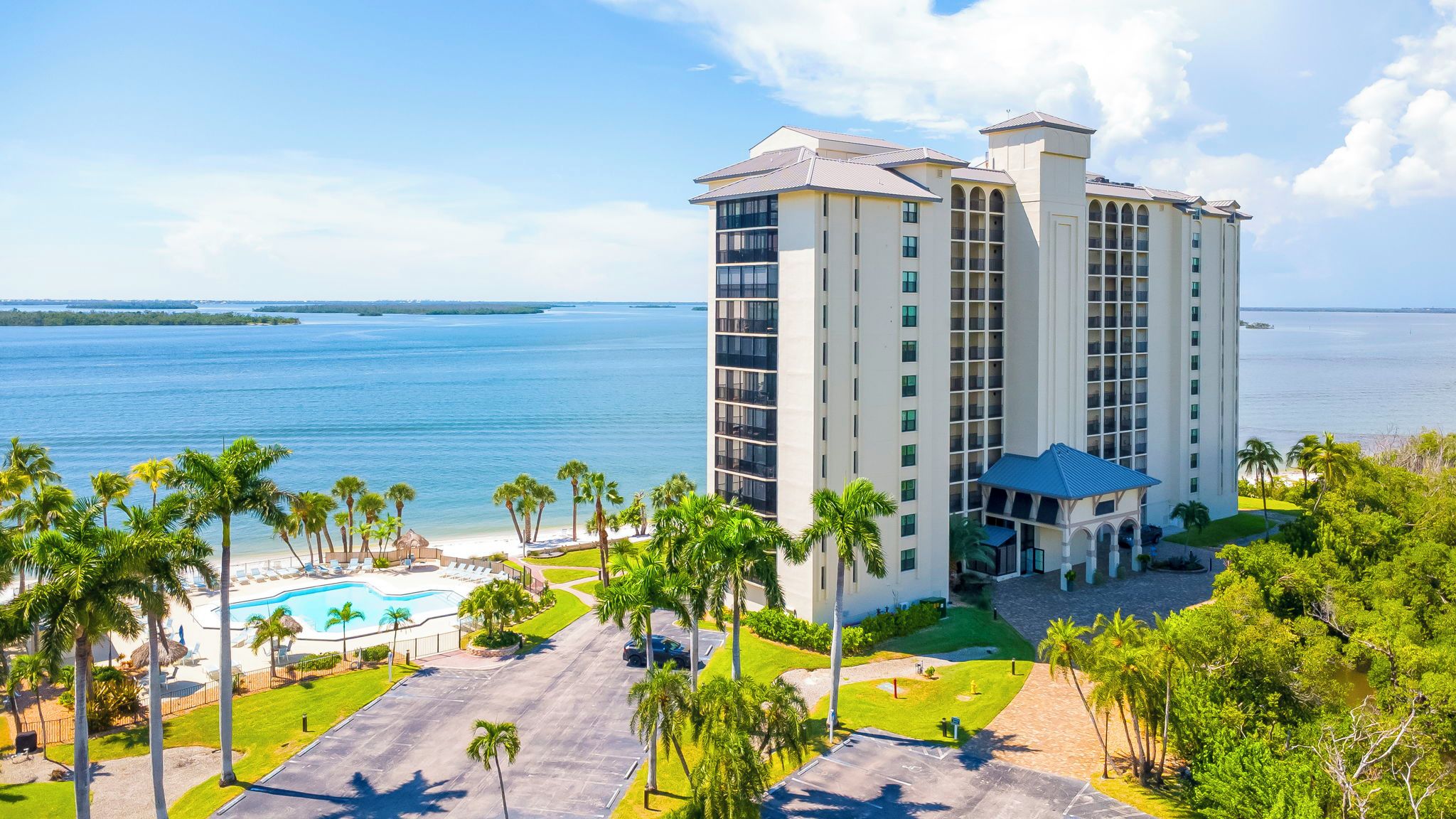 A high-rise hotel with a pool, palm trees, and a view of the ocean.