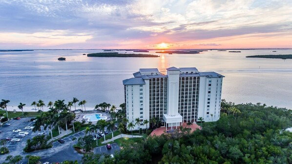 Korkea hotellirakennus, jossa on uima-allas ja josta avautuu näkymä auringonlaskuun veden yllä.