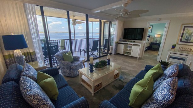 A living room with a large sofa set, a coffee table, and a TV. There is a balcony with a view of the ocean. - Sanibel Harbour Resort Harbour Tower 616      Updated luxury condo with stunning views (Fort Myers)