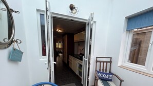 Ein Hauseingang mit einer Tür zu einer Küche, ein blauer Stuhl mit einem 'HOME'-Schild und ein hölzerner Stuhl mit Kissen.