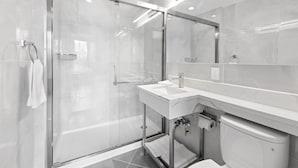A modern bathroom with a glass-enclosed shower, a white sink, and a large mirror. - Hotel 365 Bronx (Bronx)