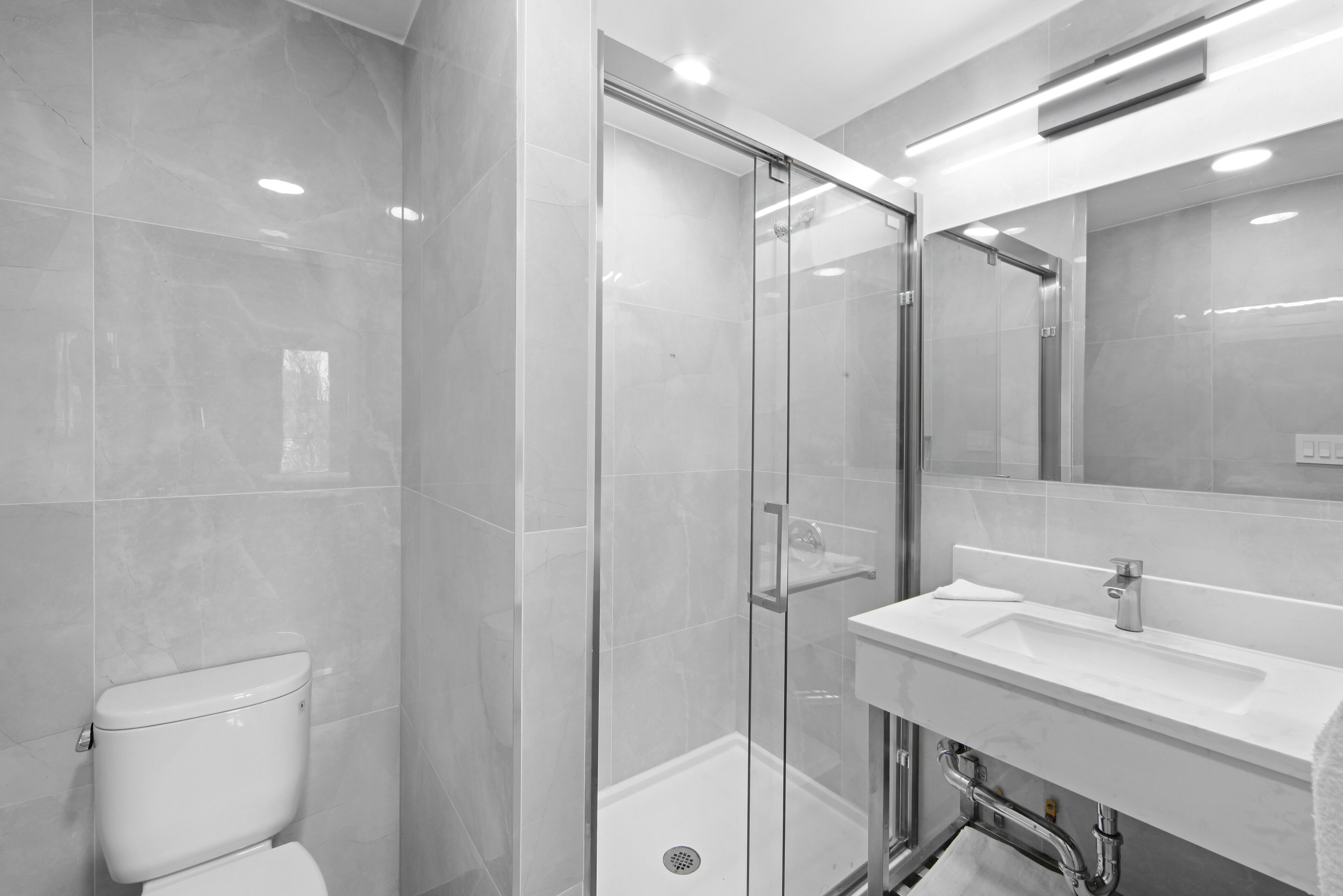 A modern bathroom with a glass-enclosed shower, a white sink, and a toilet.