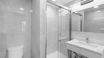 A modern bathroom with a glass-enclosed shower, a white sink, and a toilet.