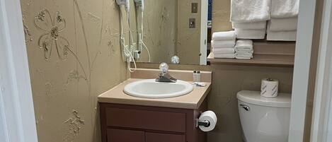 Ein Badezimmer mit Waschbecken, Spiegel, Haartrockner und Toilette.