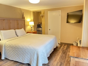 Habitación de hotel con cama, mesita de noche con lámpara, microondas, refrigerador y televisor montado en la pared.