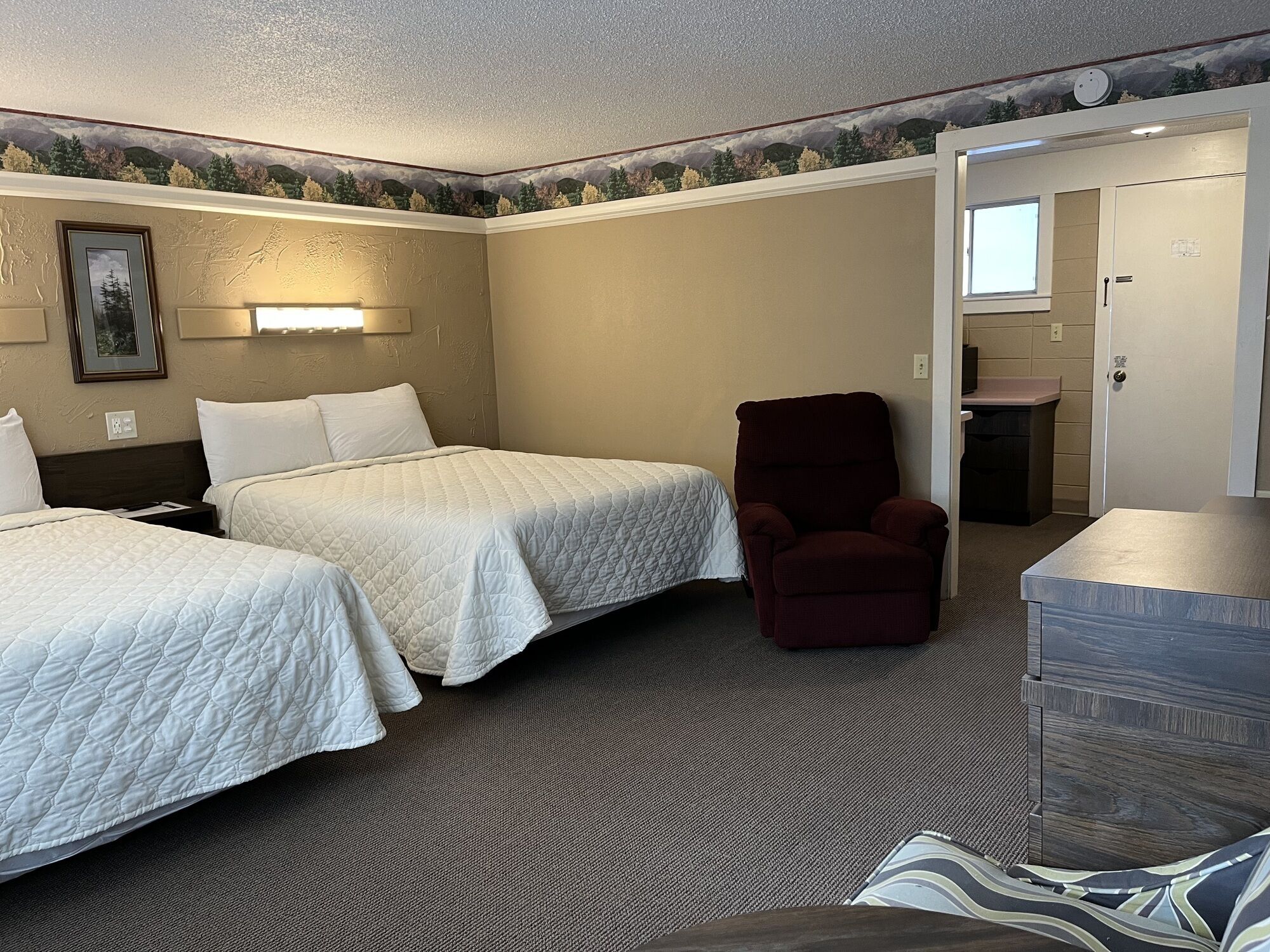 Une chambre d’hôtel avec deux lits, une chaise, un bureau et une salle de bain visible à travers une porte ouverte.