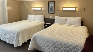 A hotel room with two queen beds, a framed picture on the wall, and a door to the left.