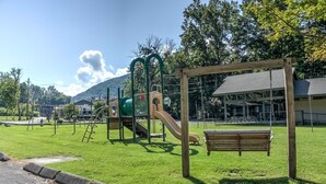 A playground with a slide and swings, a bench, and a building in the background.