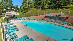 A swimming pool with blue water, surrounded by lounge chairs and a covered area with a roof.