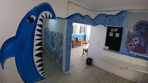 A room with a blue shark mural, a wall with a floral painting, and a sign for Cantinho Cafe. - Soul do Mar Hostel (Cabo Frio)