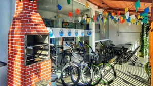 A brick outdoor grill, bicycles, and a patio area with colorful flags. - Soul do Mar Hostel (Cabo Frio)