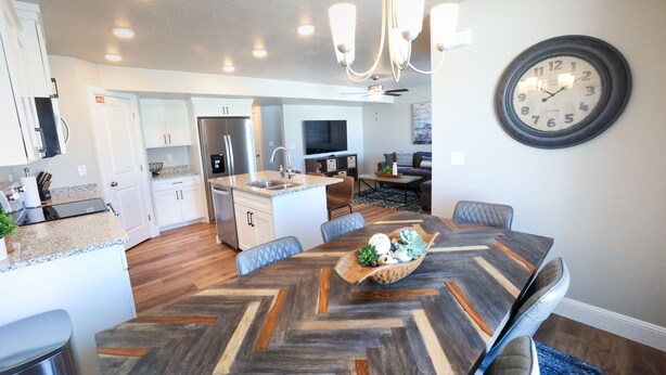 A modern kitchen with white cabinets, a central island, and a dining area with a large wooden table.