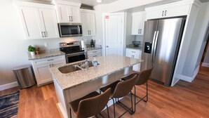 A modern kitchen with white cabinets, stainless steel appliances, a granite countertop, and a central island with bar stools.