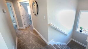 A carpeted hallway with a handrail, a door, and a window with a plant.