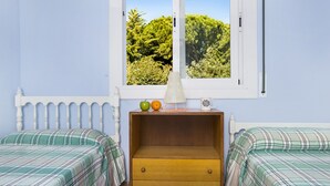 A bedroom with two beds, a wooden nightstand, a window with a view of trees, and a lamp. - 1ROCM 1D - Apartment for 5 people with terrace just 150m from the beach of Calella de Palafrugell (Calella de Palafrugell)