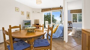 A dining area with a wooden table, blue cushioned chairs, a bowl, and a television displaying a landscape. - 1ROCM 1D - Apartment for 5 people with terrace just 150m from the beach of Calella de Palafrugell (Calella de Palafrugell)