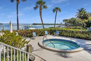 A pool area with a hot tub, lounge chairs, and a view of the water.