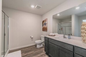 Une salle de bain moderne avec une douche à parois de verre, des toilettes, un meuble-lavabo avec un grand miroir et un plancher en bois.