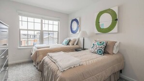 Quarto de hotel com duas camas, uma janela, cômoda e obras de arte na parede.