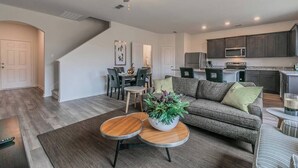 Uma sala de estar moderna com um sofá cinza, uma mesa de centro e um espaço de jantar com cadeiras e uma mesa.