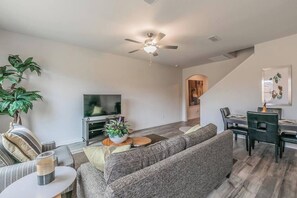 A modern living room with a sofa, TV, and dining area.