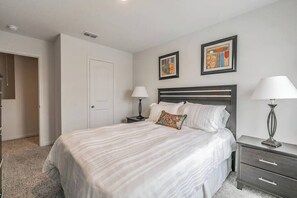 Une chambre à coucher avec un grand lit, deux tables de chevet avec des lampes, une porte et deux œuvres d’art encadrées accrochées au mur.