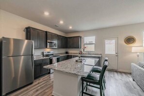 A modern kitchen with dark cabinets, stainless steel appliances, and a granite countertop island.