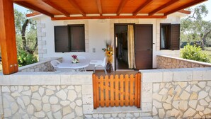 Un espace extérieur aménagé, abrité et doté d’un mur en pierre, d’une pergola en bois et d’une vue sur la maison.