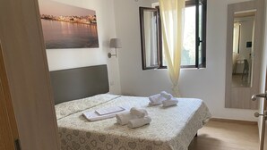 Une chambre d’hôtel avec un lit, une fenêtre avec des rideaux, une lampe fixée au mur et un tableau représentant un paysage urbain.