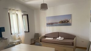 Une pièce moderne et bien éclairée, comprenant une table à manger, des chaises, un canapé et un tableau représentant un paysage côtier.