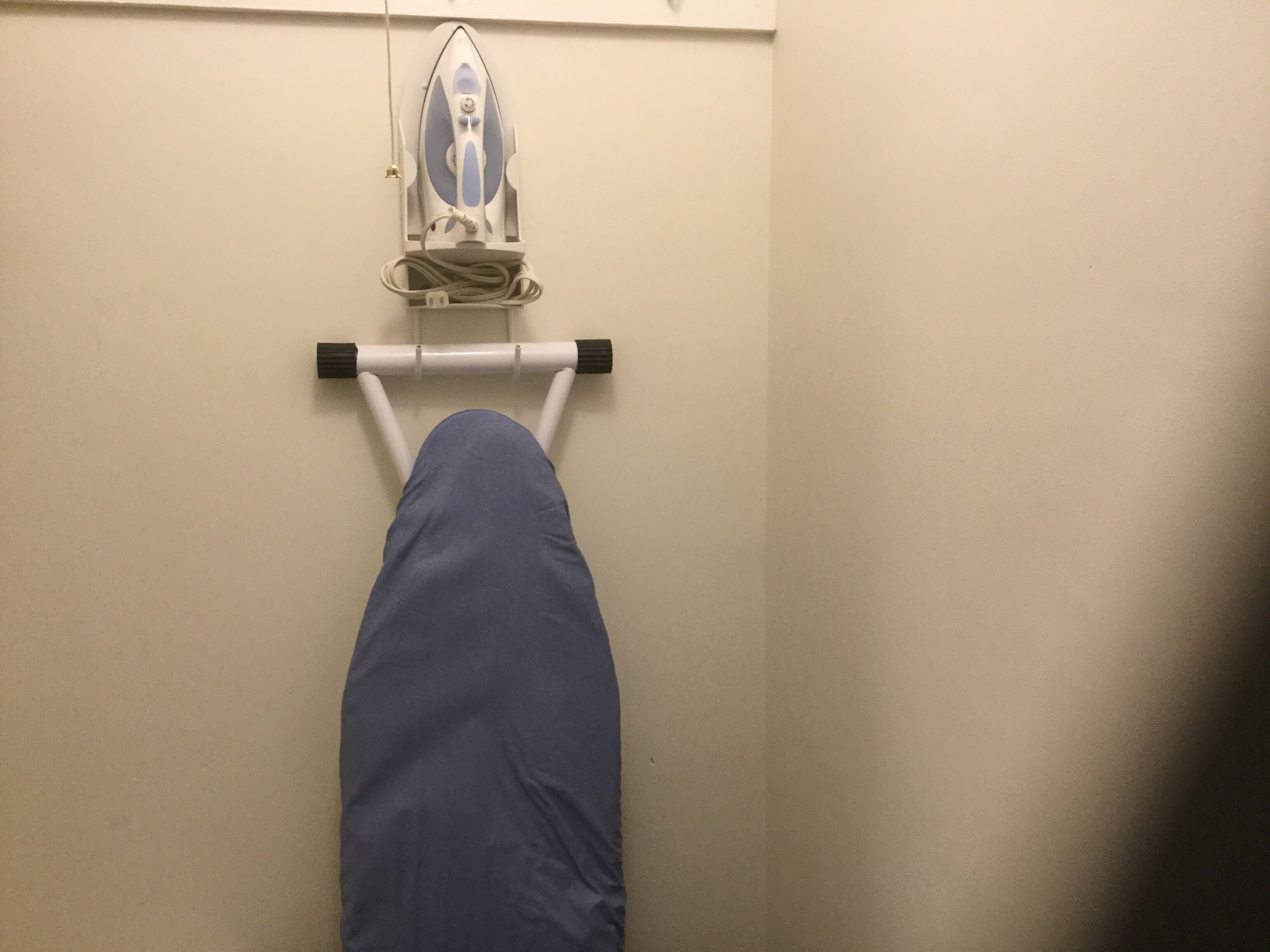 A bed with a blue blanket, a wall-mounted iron, and a white wall.