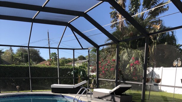 A covered swimming pool with a tiled edge, a ladder, and lounge chairs. - Cheerful 3 bedroom house with a heated pool (Naples)